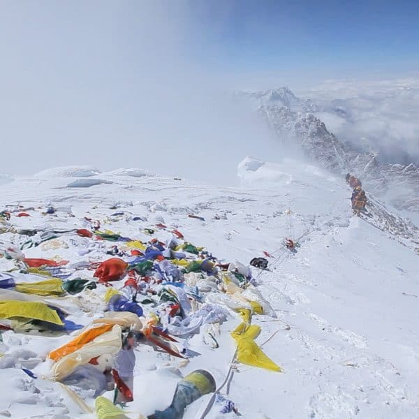 Multi coloured prayer flags mark the summit of Mt Everest as a team of climbers approach the top with mountains and clouds below in the distance