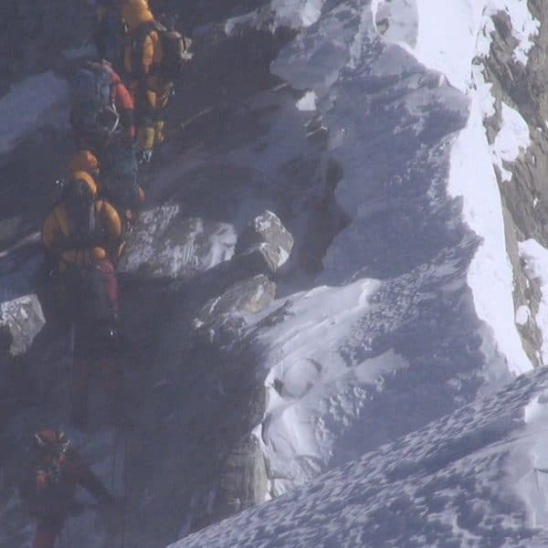 A team of climbers breating supplemental oxygen through a mask dressed in multi coloured down siuits climb a rocky section below the Hillary Step on Mt Everest