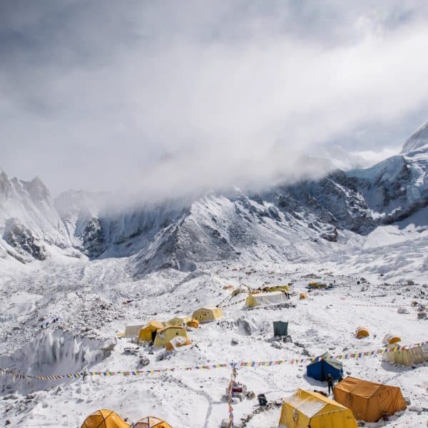 A large basecamp with multi colored tents with clouds and mountains in the background