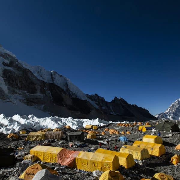 Dozens of yellow tents set up on a rock glacier with mountains in the distance and ice pinnacles