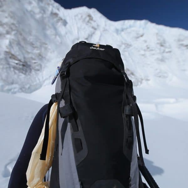 A climber walks on a snowy glacier carrying a backpack surrounded by mountains