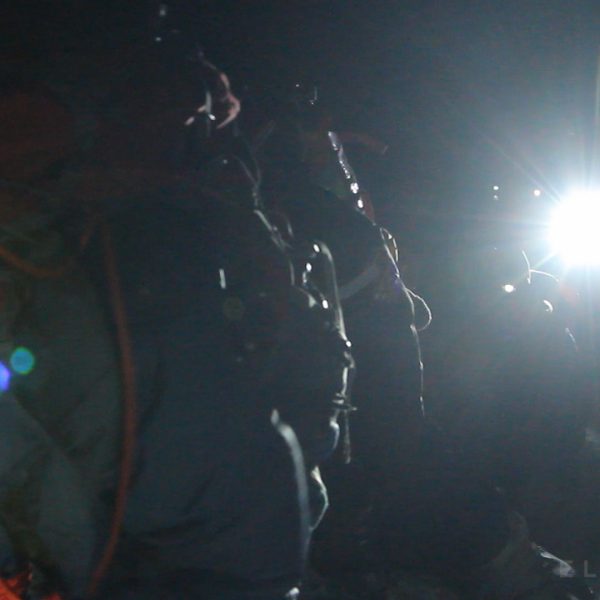 Climbers seen in silhouette as a headlamp flashes into the camera