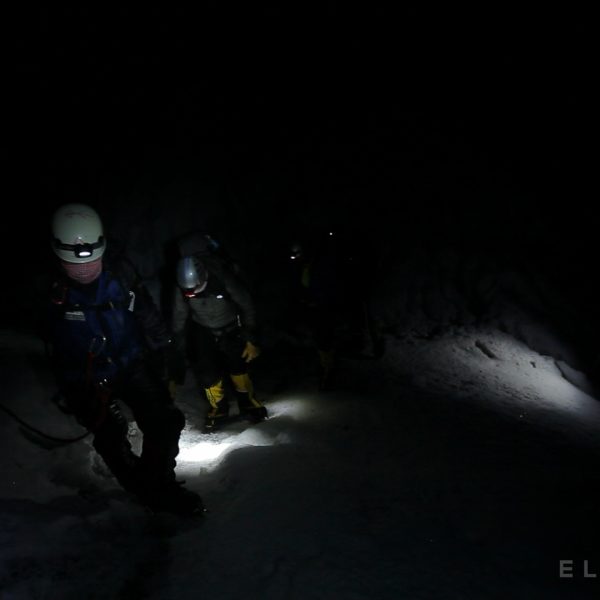 Climbers walk in the dark with headlamps on a snowy glacier