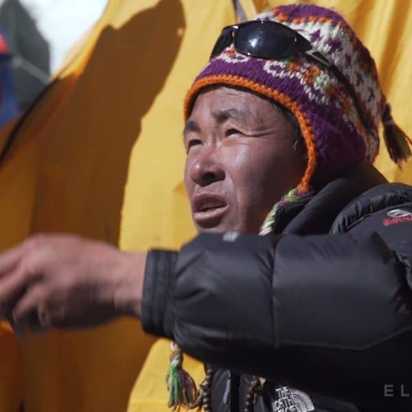 A Sherpa man holds rice in his hand in front of a yellow tent and prepares to toss it in the air