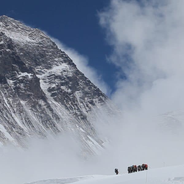 A team of climbers stand at the foot of Mt Everest with clouds and a vibrant blue sky