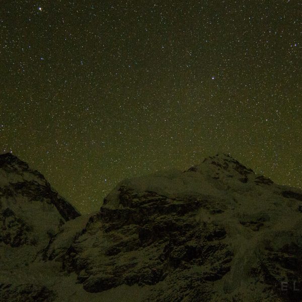 A starry night sky with two large mountains below int he shadows