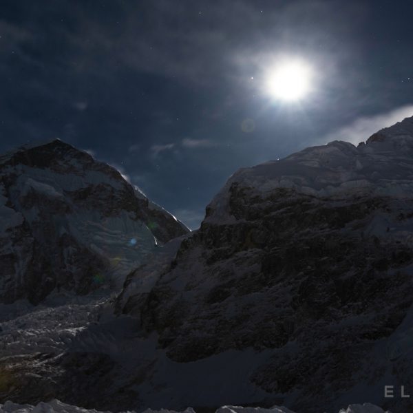 Moon rising above a glacier and two snow capped mountains with a deep blue sky int he background
