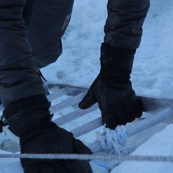 Close up of hads and feet wearing boots and gloves crossing a ladder in a snowy area