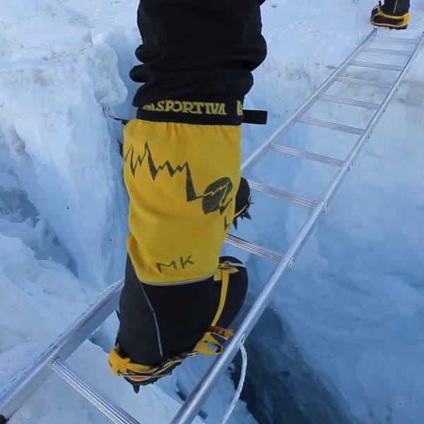 A close up shot of a climbers yellow boots crossing an aluminim ladder suspended over a crevasse