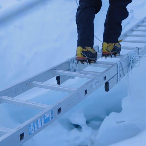 Close up of yellow boots walking on an aluminum ladder in a snowy setting