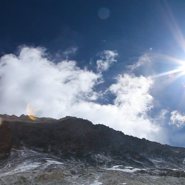 The sun shines high over a rocky mountain called Everest with clouds near the summit