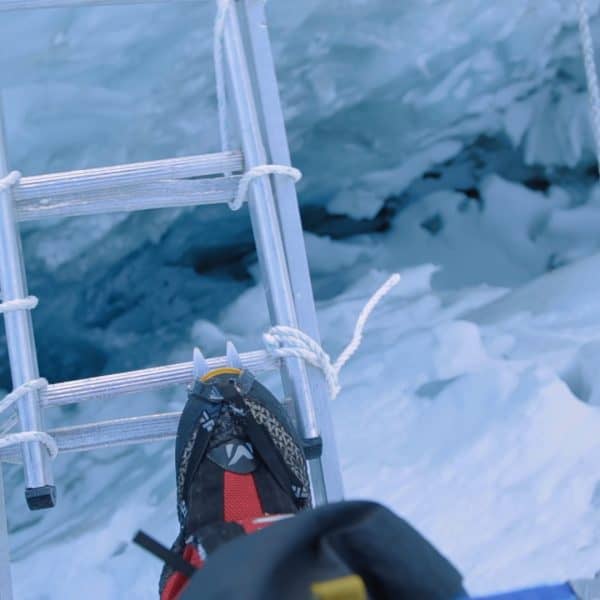 Close up of a boot with spikes on it while stepping onto an aluminum ladder suspended over a crevasse