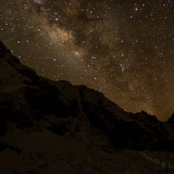 Milky Way above two mountains on a starry night with tents lit up with head torches