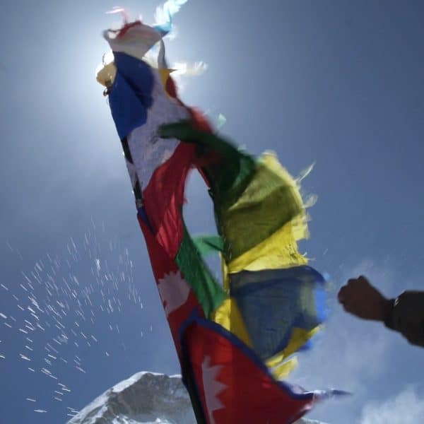 A Sherpa man tossed rice in the air towards a tall multi colored prayer flag