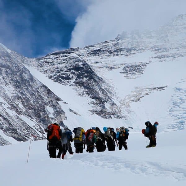 8 climbers walk on a snowy glacier with a steep mountain in the distance