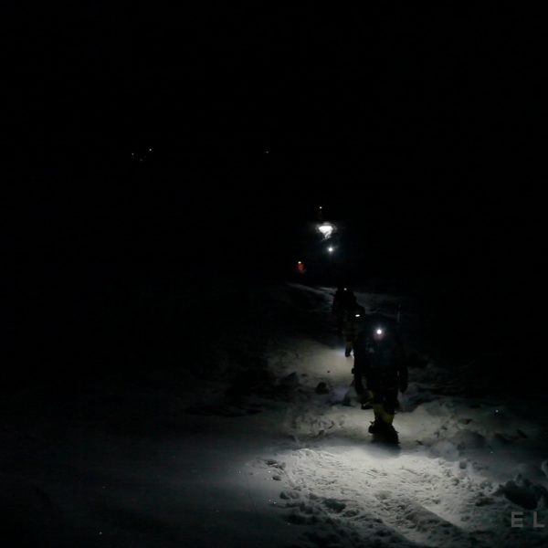 Climbers walk in the dark with headlamps on a snowy glacier carrying ice axes