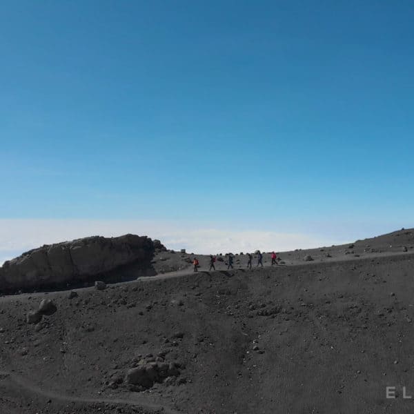 6 Climbers walk down a path above the clouds on Kilimanjaro mountain on a dry rocky trail