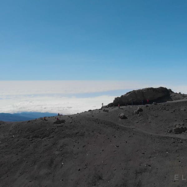 6 Climbers walk down a path above the clouds on Kilimanjaro mountain on a dry rocky trail