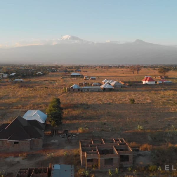 An Afrcian village surrounded by dry fields with two tall mountains in the distance including Mt Kilimanjaro